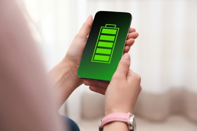 Image of Young woman holding smartphone with fully charged battery indoors, closeup