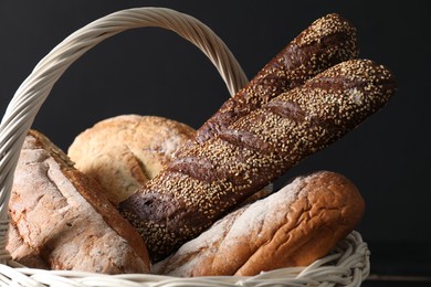 Photo of Wicker basket with different types of fresh bread on dark background, closeup