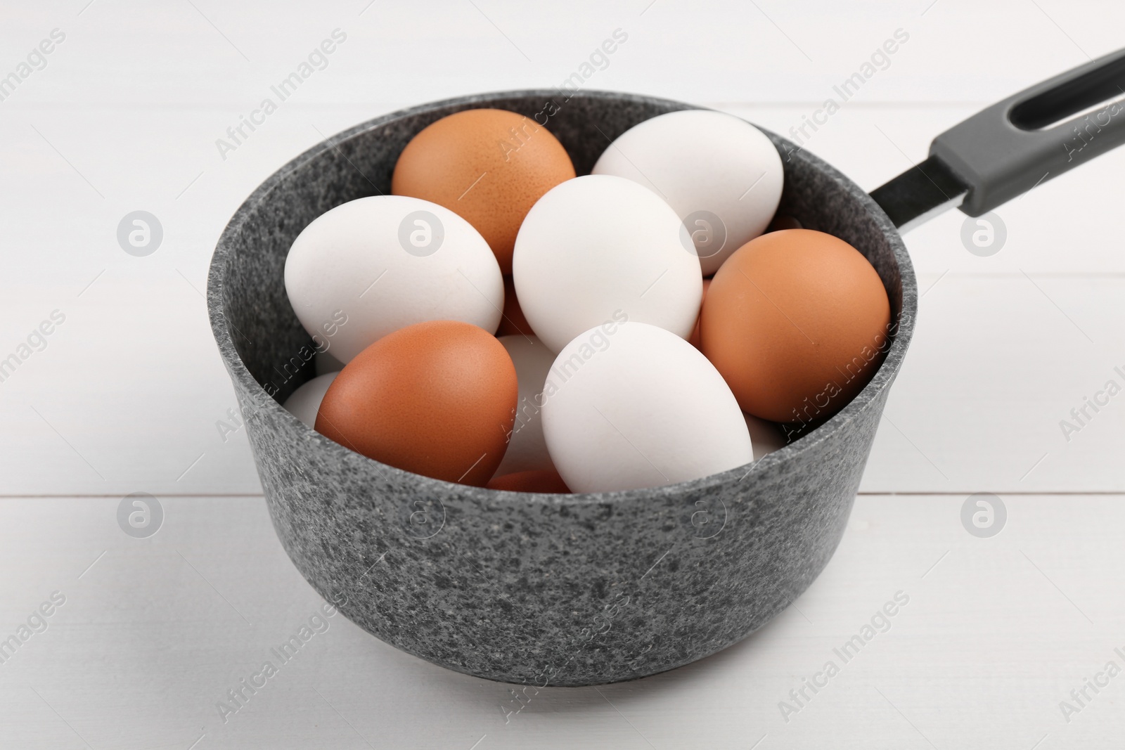 Photo of Unpeeled boiled eggs in saucepan on white wooden table, closeup