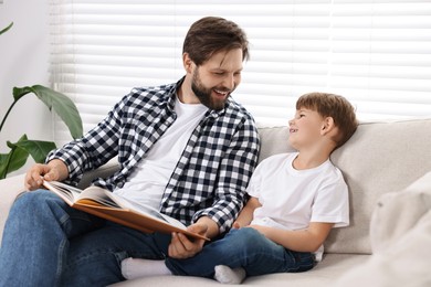 Happy dad and son reading book together on sofa at home
