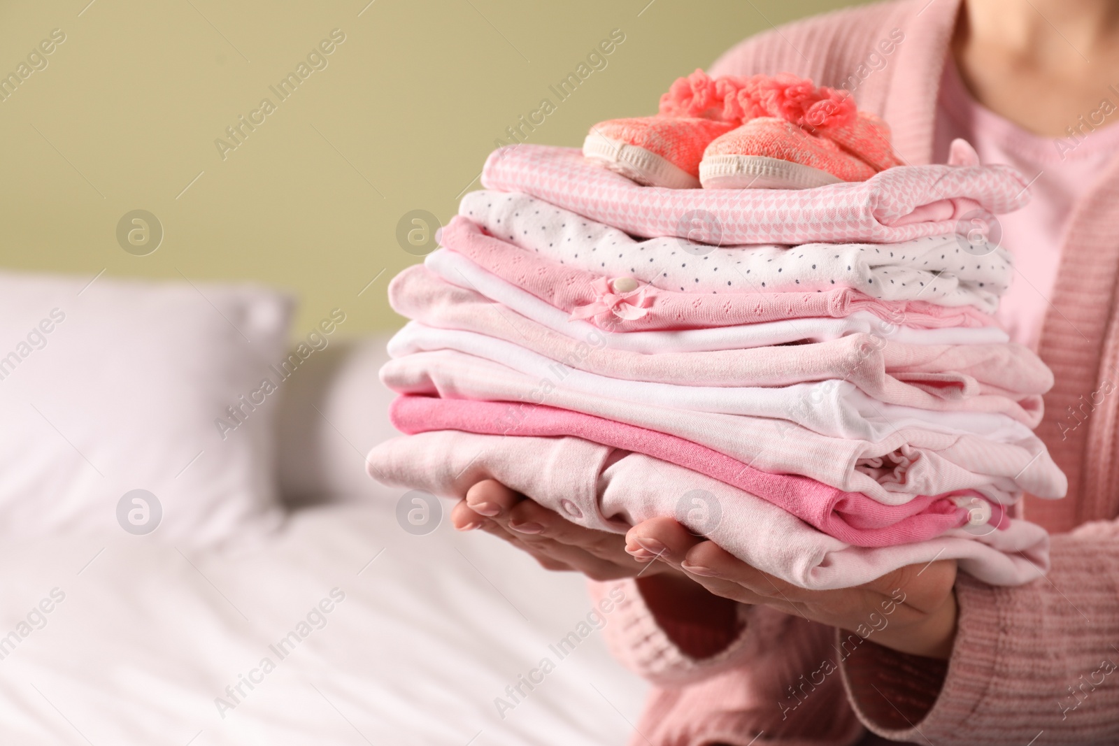 Photo of Woman holding stack of baby girl's clothes with shoes indoors, closeup. Space for text