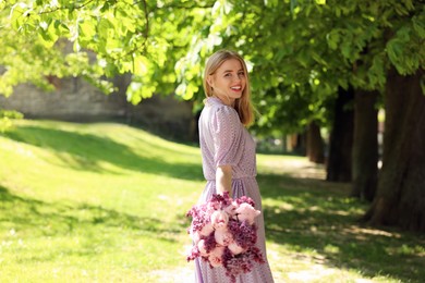 Beautiful woman with bouquet of spring flowers in park on sunny day