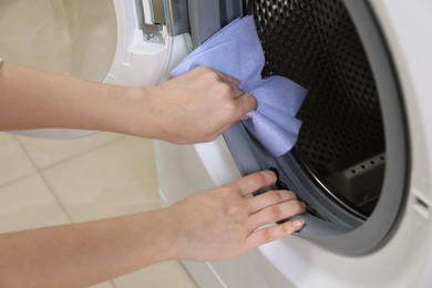 Photo of Woman cleaning empty washing machine with rag, closeup