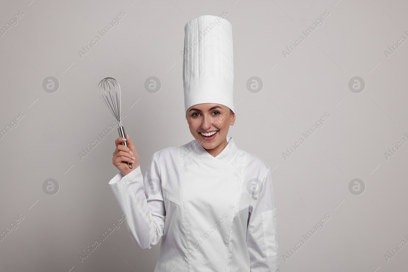 Photo of Happy professional confectioner in uniform holding whisk on light grey background