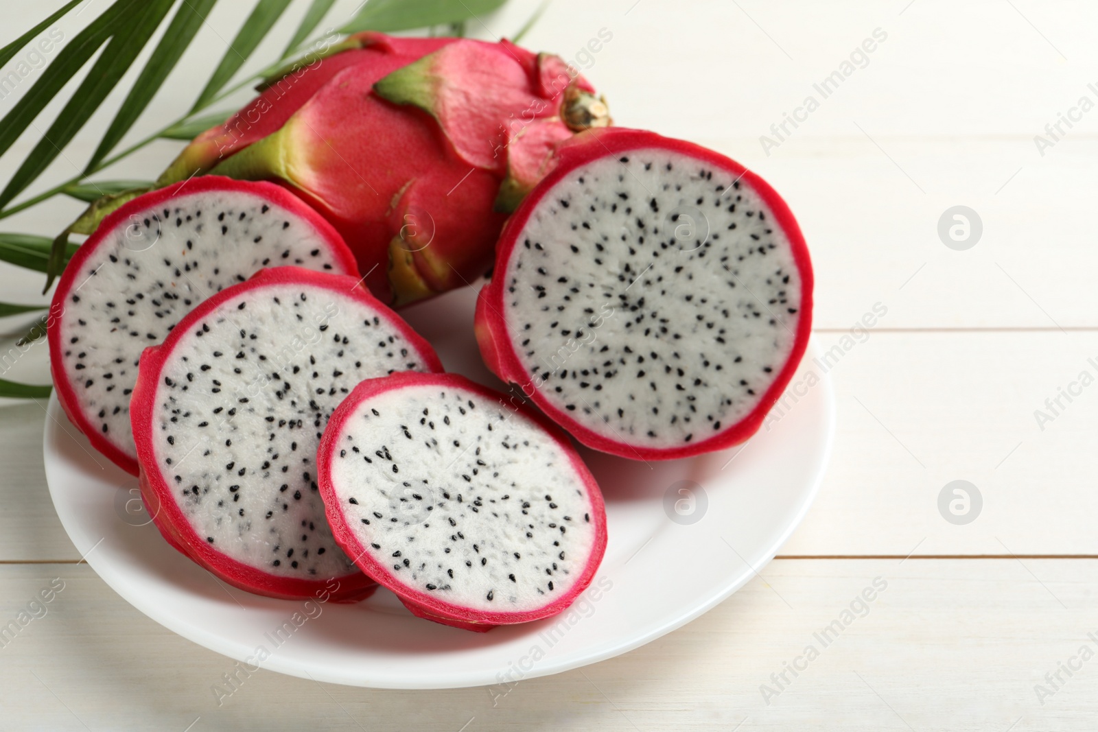 Photo of Plate with delicious cut and whole pitahaya fruits on white wooden table