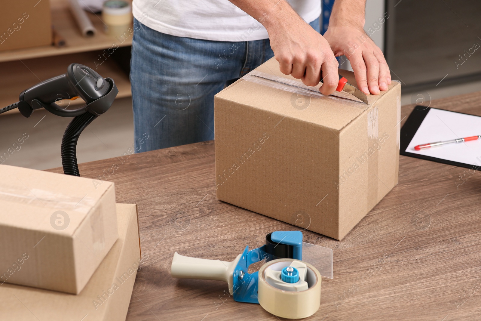 Photo of Post office worker with utility knife opening parcel at counter indoors, closeup