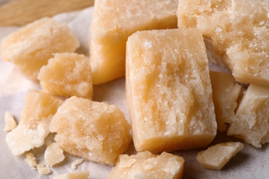 Photo of Pieces of delicious parmesan cheese on parchment, closeup view