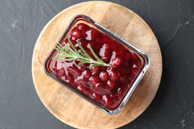 Photo of Fresh cranberry sauce and rosemary in glass bowl on gray textured table, top view