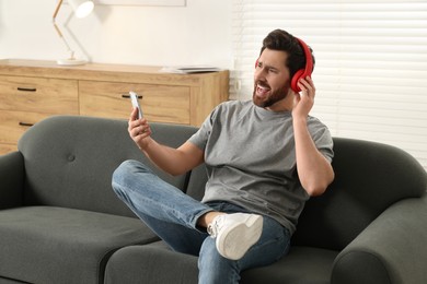 Photo of Emotional man listening music with headphones on sofa indoors