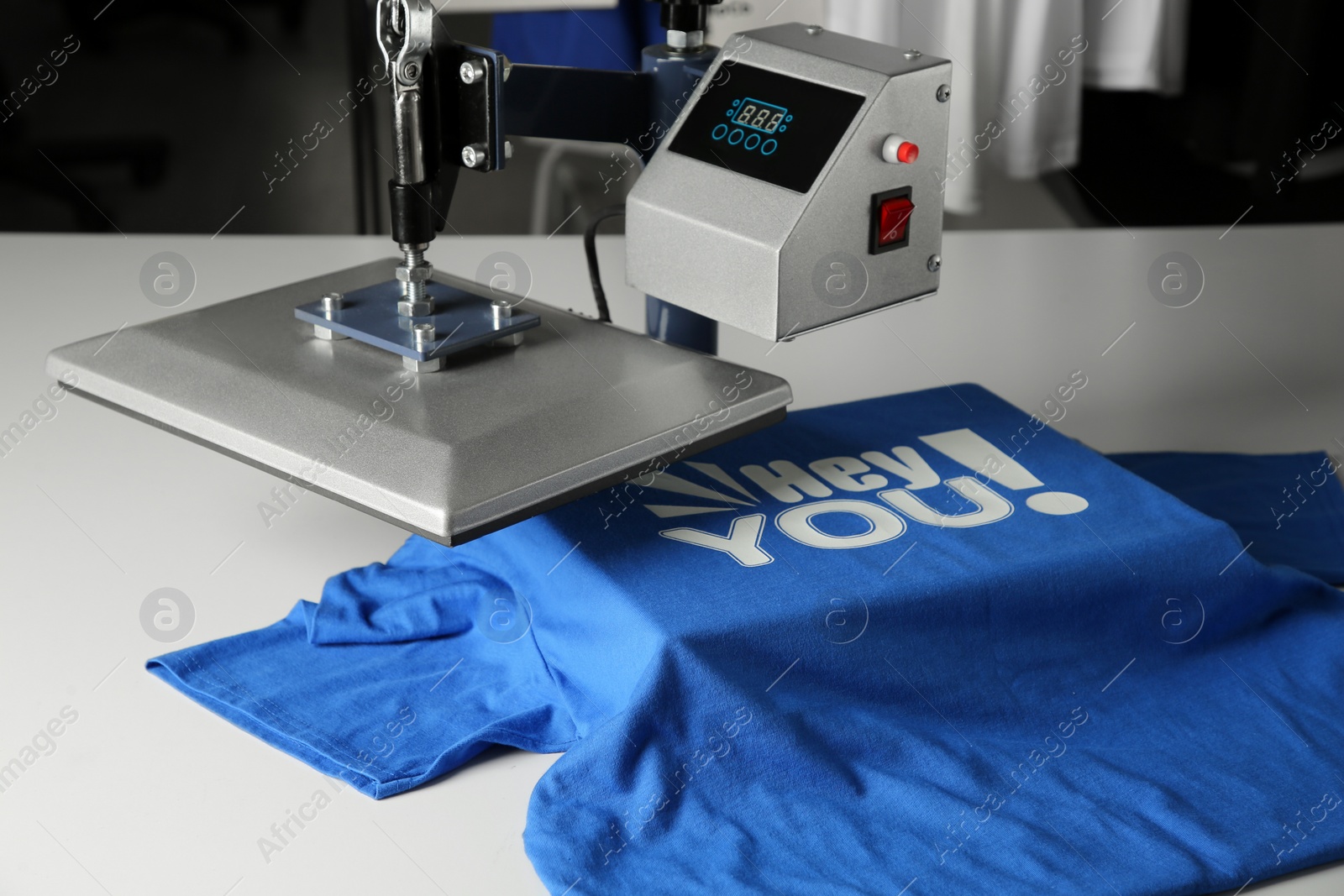 Photo of Printing logo. Heat press with blue t-shirt on white table