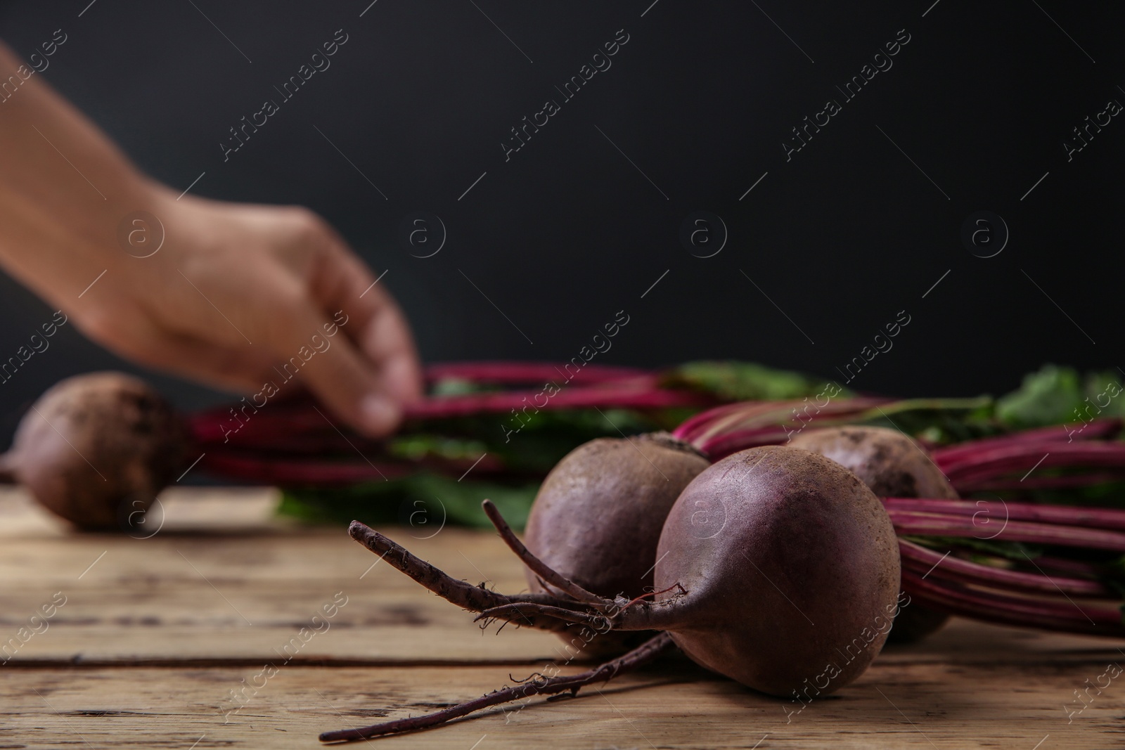 Photo of Fresh beets with leaves on wooden table against black background, closeup. Space for text