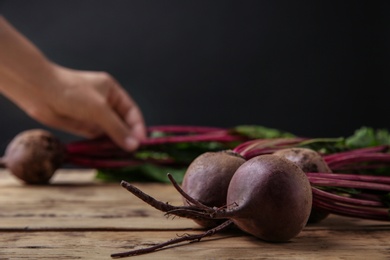 Fresh beets with leaves on wooden table against black background, closeup. Space for text