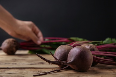 Photo of Fresh beets with leaves on wooden table against black background, closeup. Space for text