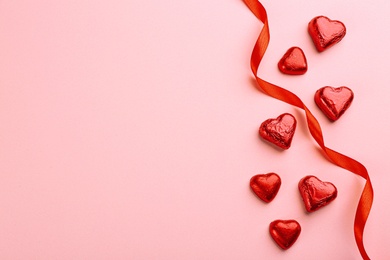 Heart shaped chocolate candies and ribbon on pink background, flat lay. Space for text