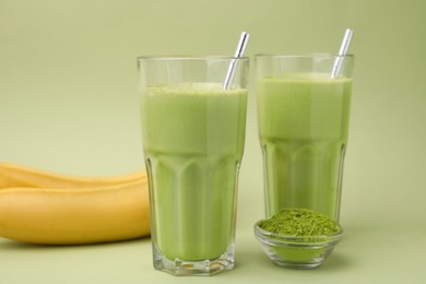 Photo of Glasses of tasty matcha smoothie and powder on pale green background