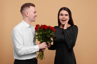 Photo of Boyfriend presenting bouquetred roses to his girlfriend on beige background. Valentine's day celebration