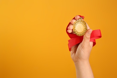 Photo of Woman holding gold medal on yellow background, closeup. Space for text
