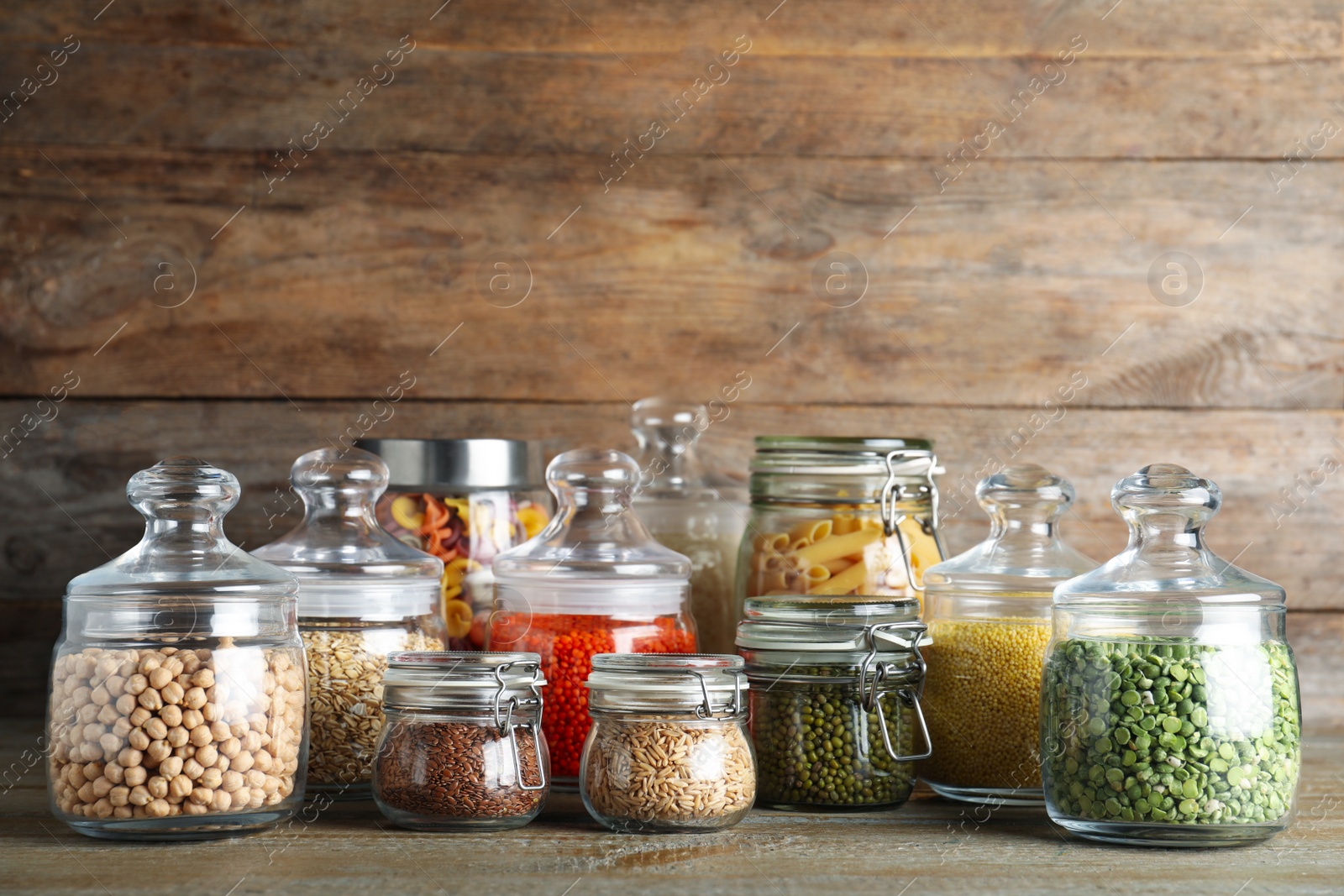 Photo of Glass jars with different types of groats and pasta on wooden table