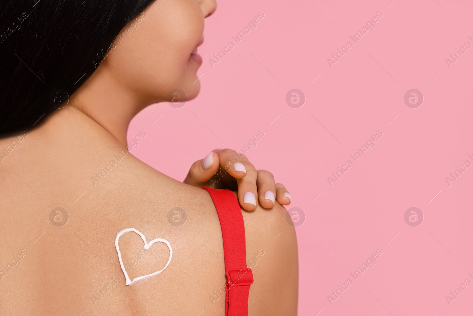 Photo of Young woman with sun protection cream on her back against pink background, closeup. Space for text