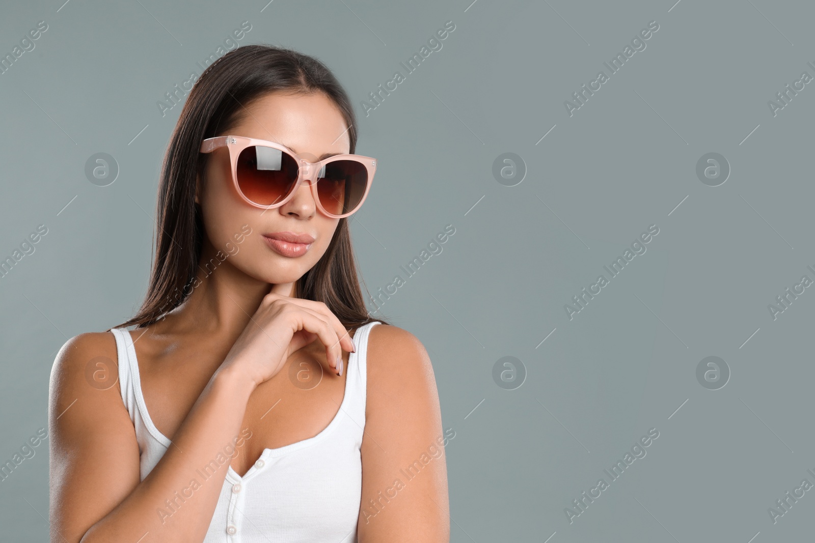 Photo of Beautiful young woman wearing sunglasses on grey background. Space for text