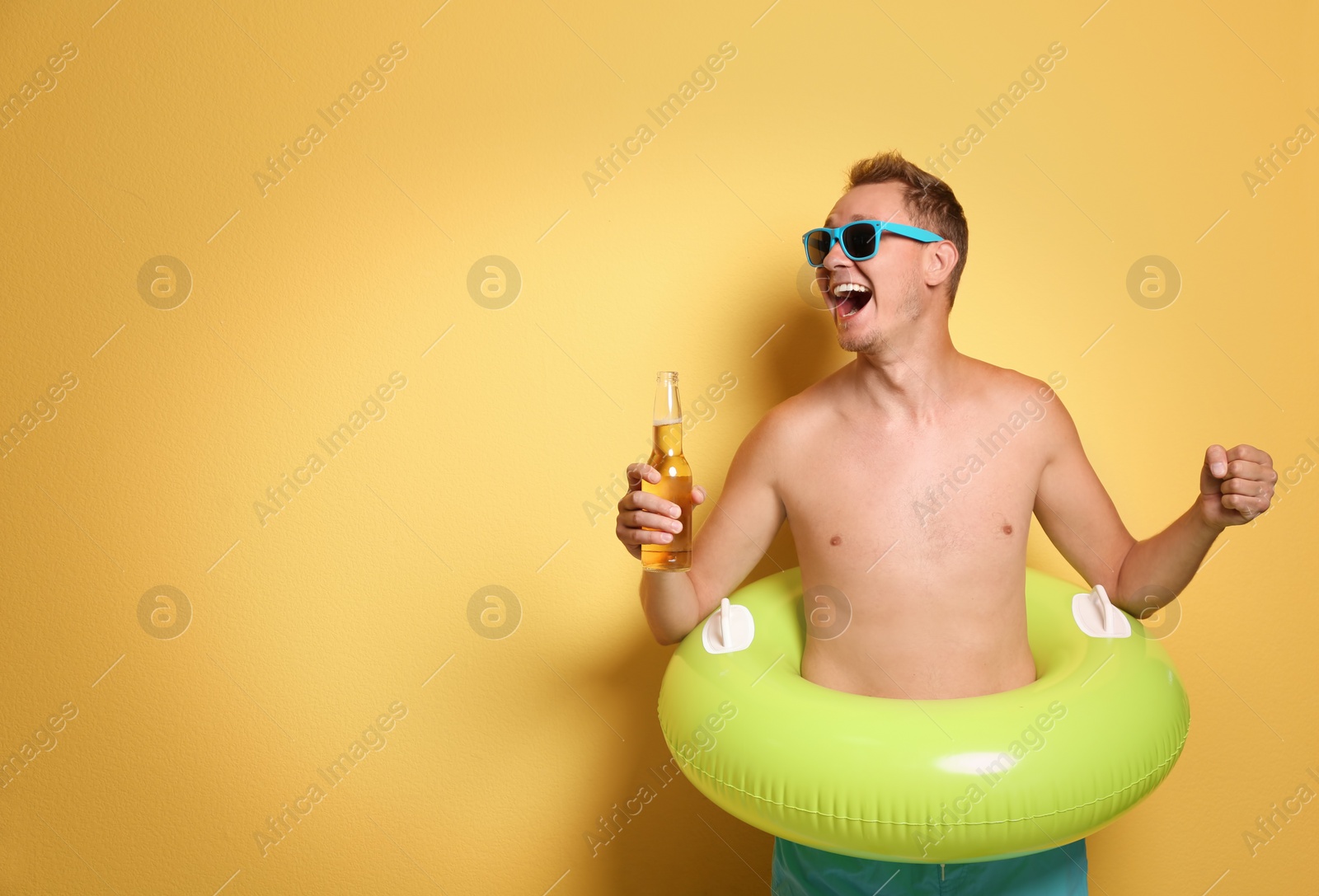 Photo of Shirtless man with inflatable ring and bottle of drink on color background