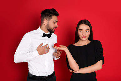 Young woman with engagement ring making marriage proposal to her boyfriend on red background