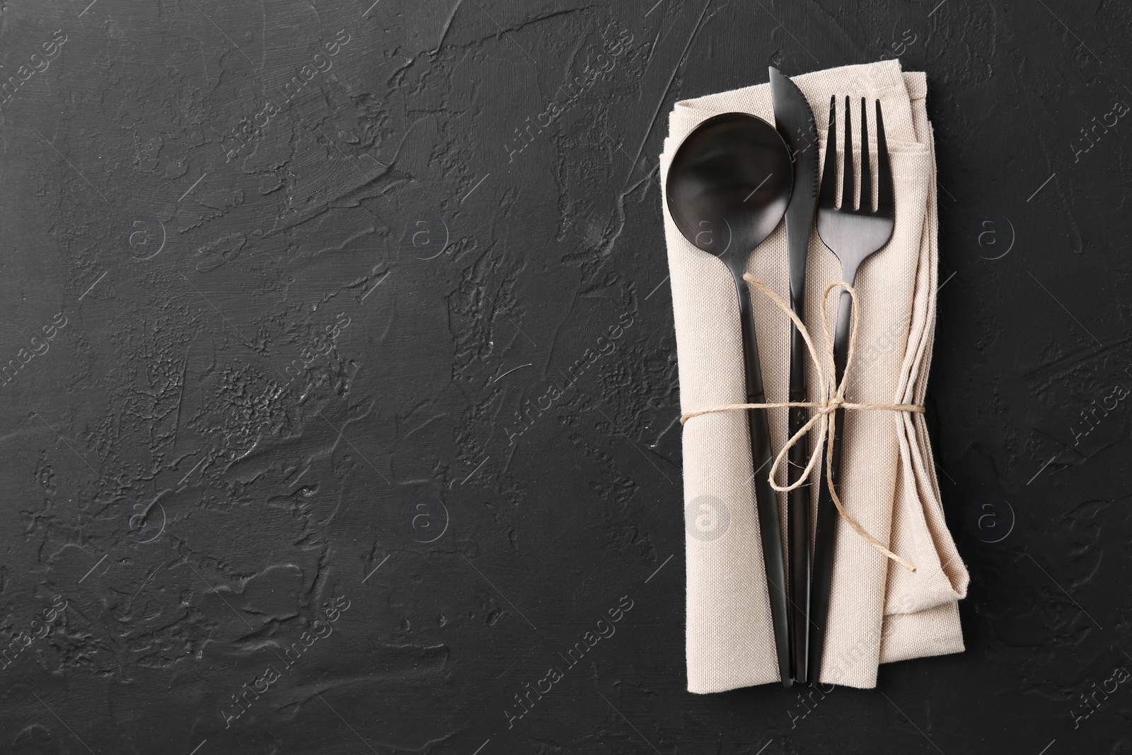 Photo of Set of stylish cutlery and napkin on black table, top view. Space for text