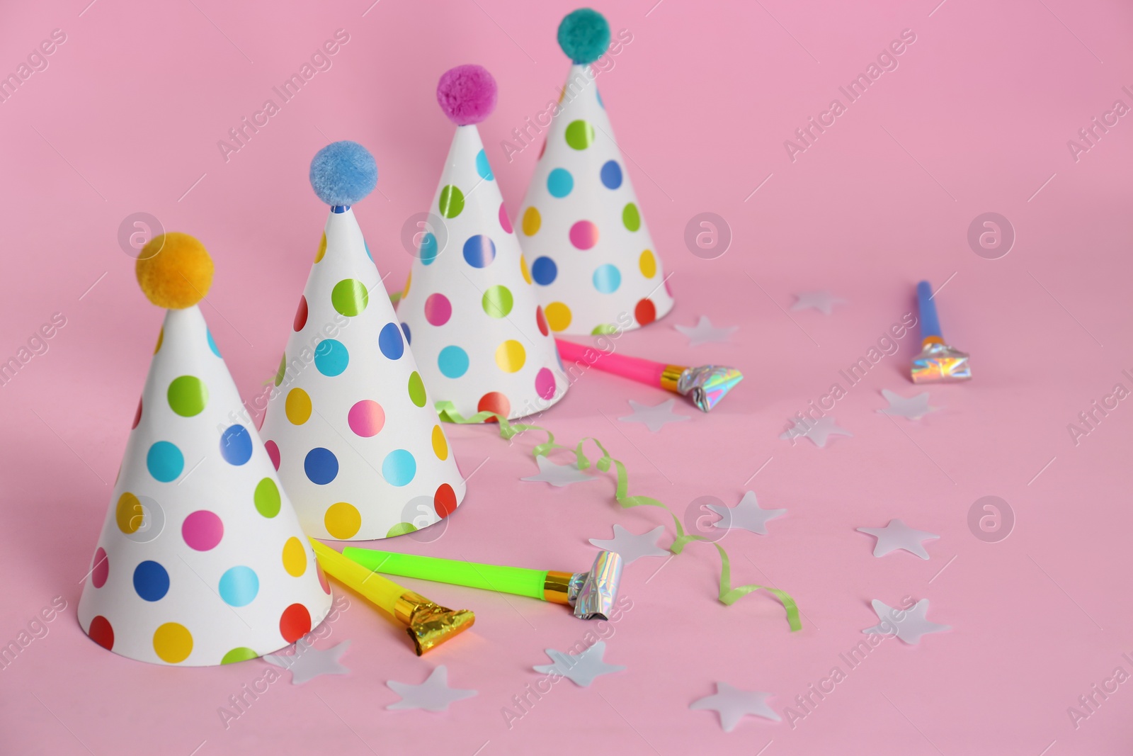 Photo of Colorful party hats with fluffy balls and blowers on pink background