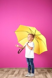 Little boy with yellow umbrella near color wall