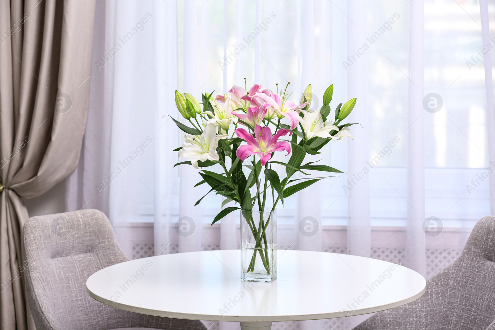 Photo of Vase with bouquet of beautiful lilies on white table indoors