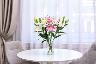 Photo of Vase with bouquet of beautiful lilies on white table indoors