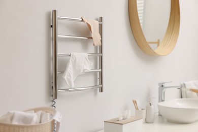 Photo of Heated towel rail with underwear on white wall in bathroom