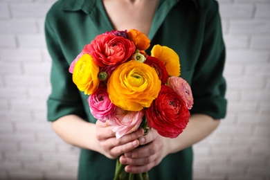 Photo of Woman holding beautiful ranunculus flowers near white brick wall, closeup