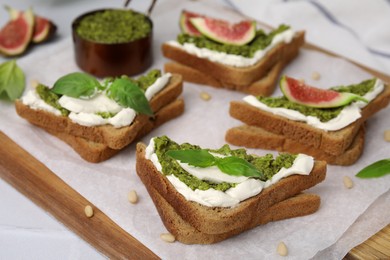 Photo of Tasty bruschetta with cream cheese, pesto sauce and fresh basil on parchment paper, closeup