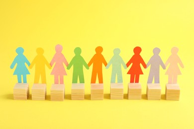 Photo of Paper human figures with wooden cubes on yellow background. Diversity and Inclusion concept