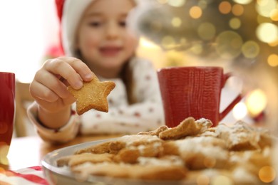 Little girl taking tasty Christmas cookie from plate at table, closeup