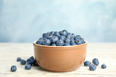 Tasty ripe blueberries in bowl on white wooden table