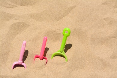 Bright plastic shovels in sand, space for text. Beach toys