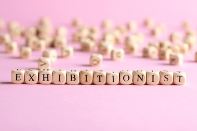 Photo of Word EXHIBITIONIST made with wooden cubes on pink background