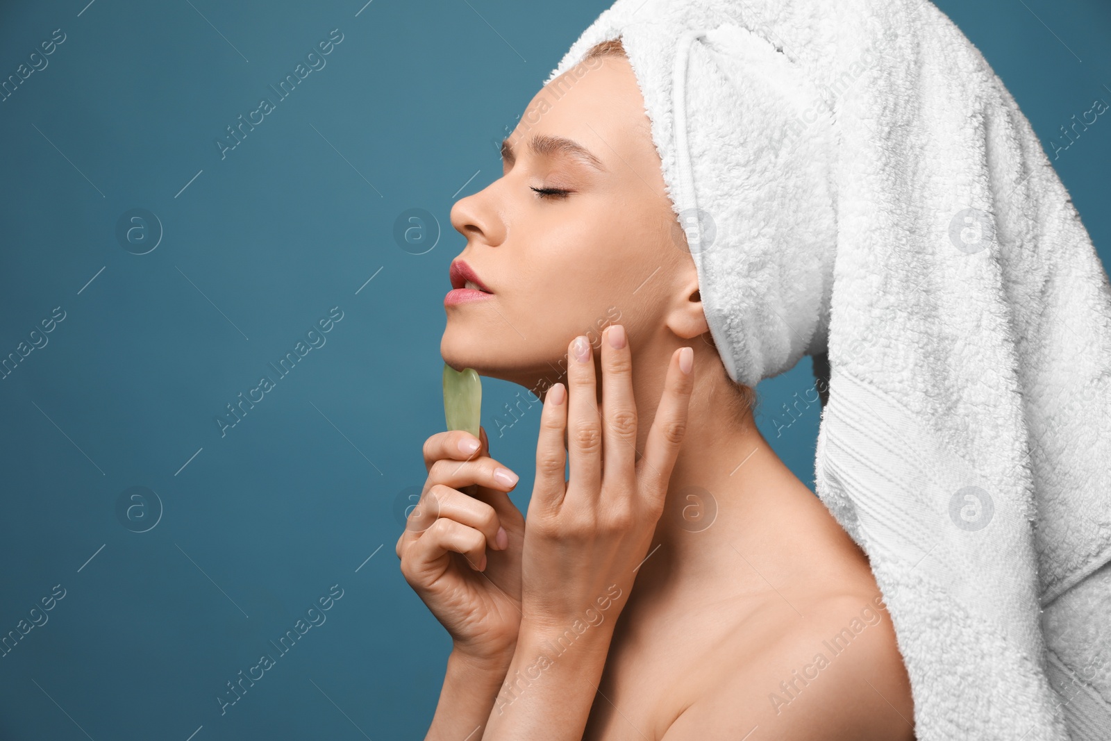 Photo of Beautiful young woman doing facial massage with gua sha tool on blue background. Space for text