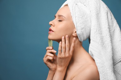 Beautiful young woman doing facial massage with gua sha tool on blue background. Space for text