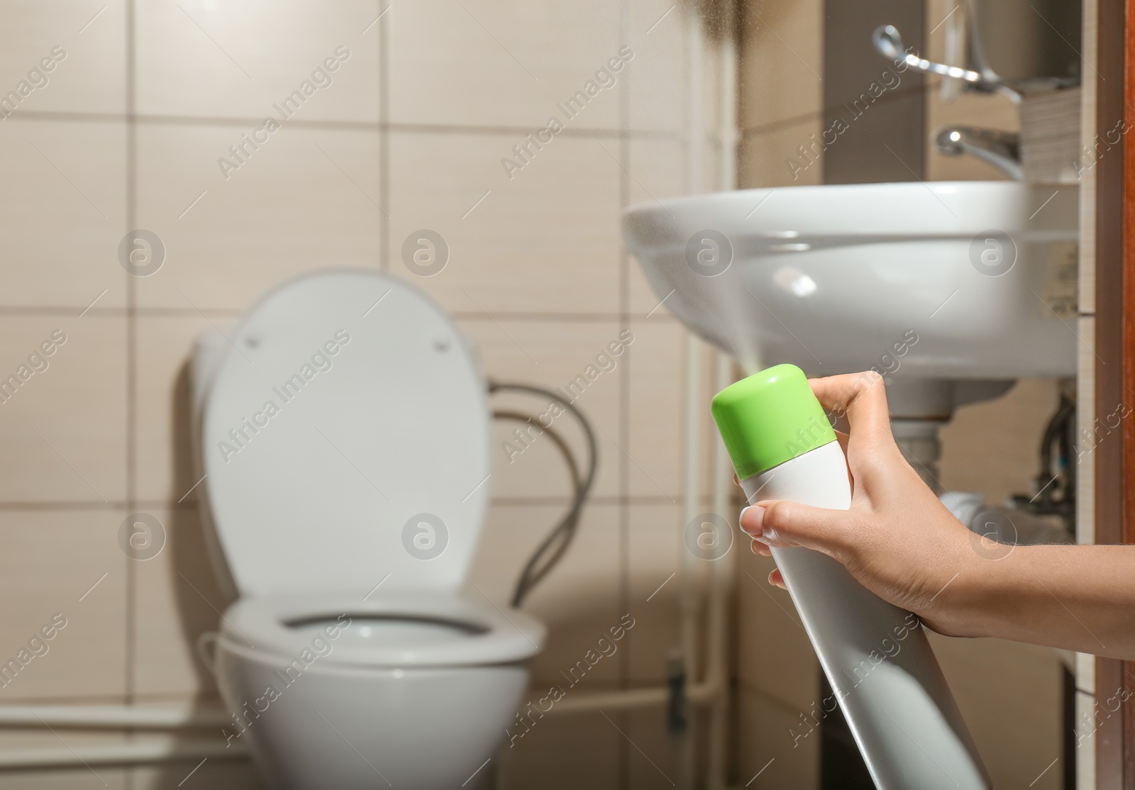 Photo of Woman spraying air freshener in bathroom