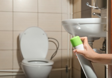Photo of Woman spraying air freshener in bathroom