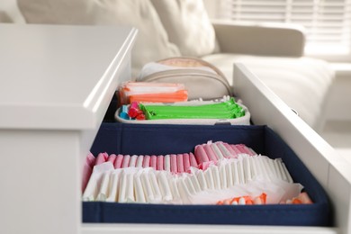 Photo of Open cabinet drawer with menstrual pads and tampons indoors, closeup