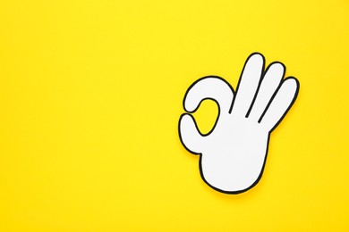 Photo of Paper cutout of okay hand gesture on yellow background, top view. Space for text