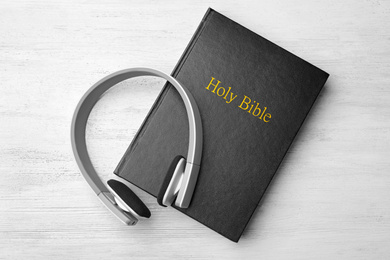 Photo of Bible and headphones on white wooden background, top view. Religious audiobook