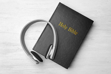 Bible and headphones on white wooden background, top view. Religious audiobook