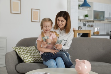 Photo of Mother and daughter counting money on sofa indoors