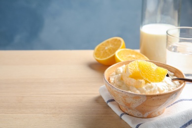 Photo of Creamy rice pudding with orange slices in bowl on wooden table. Space for text