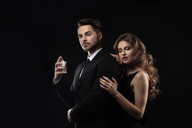 Passionate woman and handsome man using perfume on black background